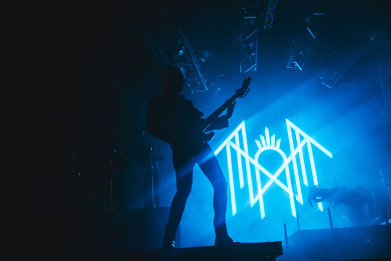 A band member playing the guitar in front of the Sleep Tokens neon blue logo