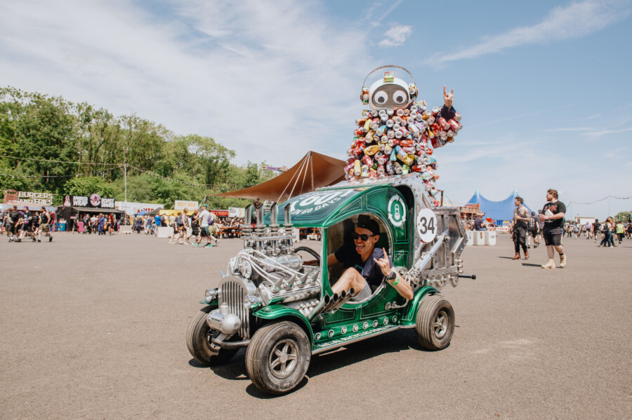 Person driving a green vehicle topped with a robot sculpture made from recycled cans.